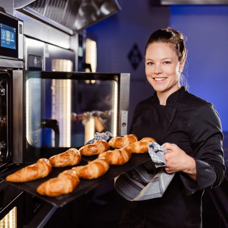 Bäckerin holt frische Croissants aus MKN Kombidämpfer in Profiküche