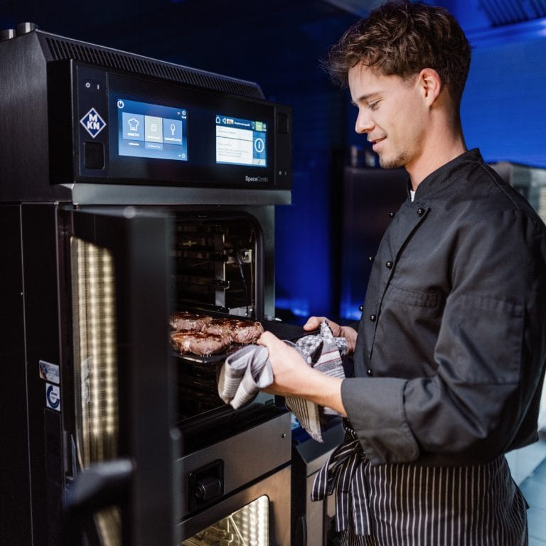 Koch entnimmt gebratenes Fleisch aus einem MKN Kombidämpfer in Profiküche